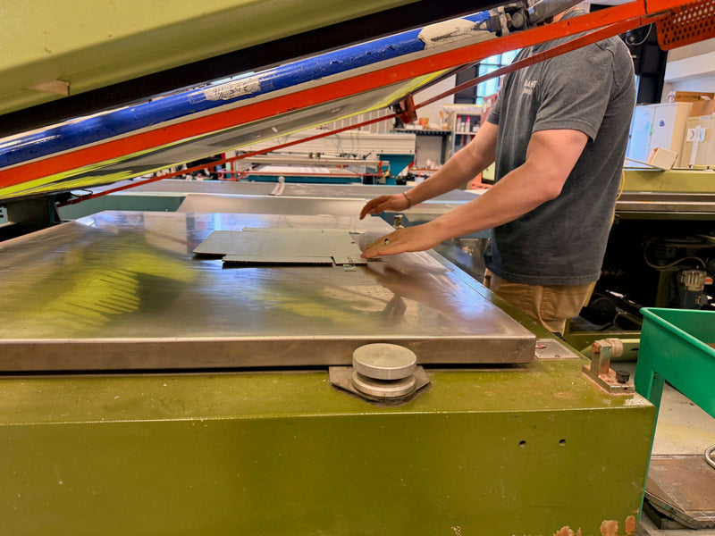 Screen printing operator positioning a sheet material substrate on an industrial silkscreen press, demonstrating the hands-on precision of the silkscreen printing process for durable industrial graphics.